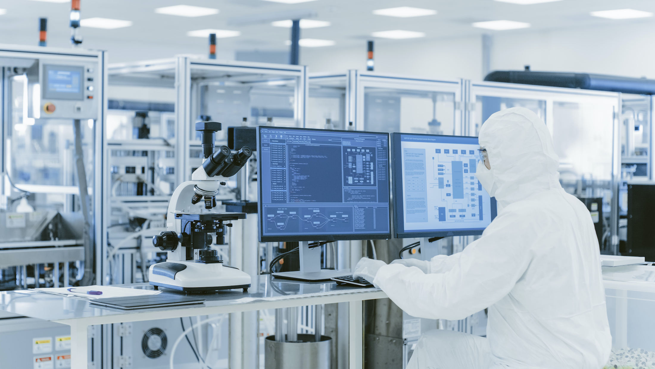 In Laboratory Over the Shoulder View of Scientist in Protective Clothes Doing Research on a Computer developing Pharmaceutical drugs.